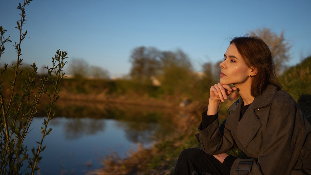 A woman sitting by a lakeside, contemplating nature during sunset.